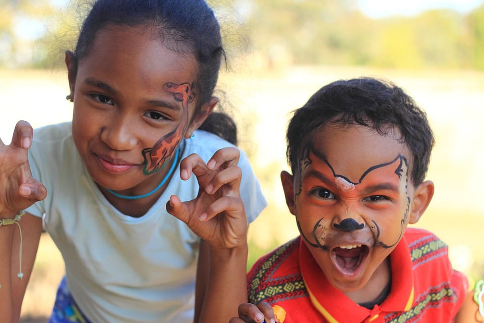 Dos niños con la cara pintada y las manos levantadas fingen ser animales. La niña tiene un tigre en la mejilla, mientras que el niño tiene la cara de un zorro pintada y hace una expresiva cara de gruñido: es la fórmula perfecta para el juego imaginativo.