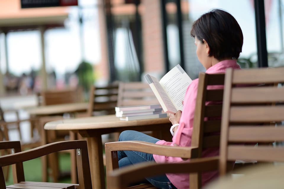 Una persona con una camisa rosa sentada en un banco al aire libre, leyendo un libro sobre la elaboración del duelo.