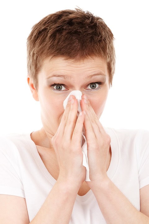 Persona con cabello corto sonándose la nariz con un pañuelo mientras usa una camisa blanca, lidiando con problemas de salud.