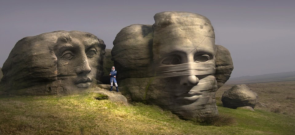 Una persona se para frente a grandes esculturas de piedra que se asemejan a rostros humanos en un entorno cubierto de hierba, contemplando el arte mientras busca alivio de su malestar psicológico.