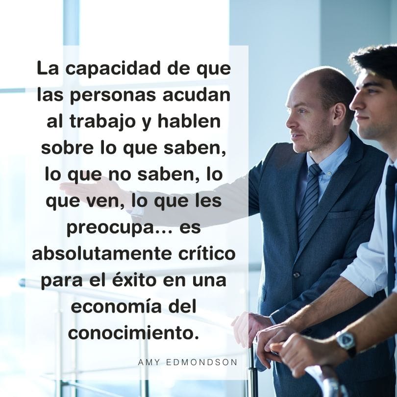 Tres personas en trajes formales observan algo fuera de la imagen desde lo alto de un edificio mientras una cita de Amy Edmondson sobre la importancia de la Seguridad Psicológica y el conocimiento en la economía aparece en primer plano.