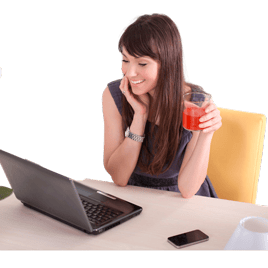 Una mujer sonríe mientras mira su computadora portátil, sosteniendo un vaso de bebida roja en la mano. Sobre la mesa a su lado hay un teléfono inteligente mientras espera su sesión de terapia online..