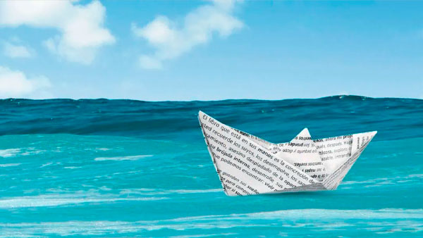 Un barco de papel hecho a partir de una página de texto impresa de libros antiguos flota en un océano azul y tranquilo bajo un cielo parcialmente nublado.