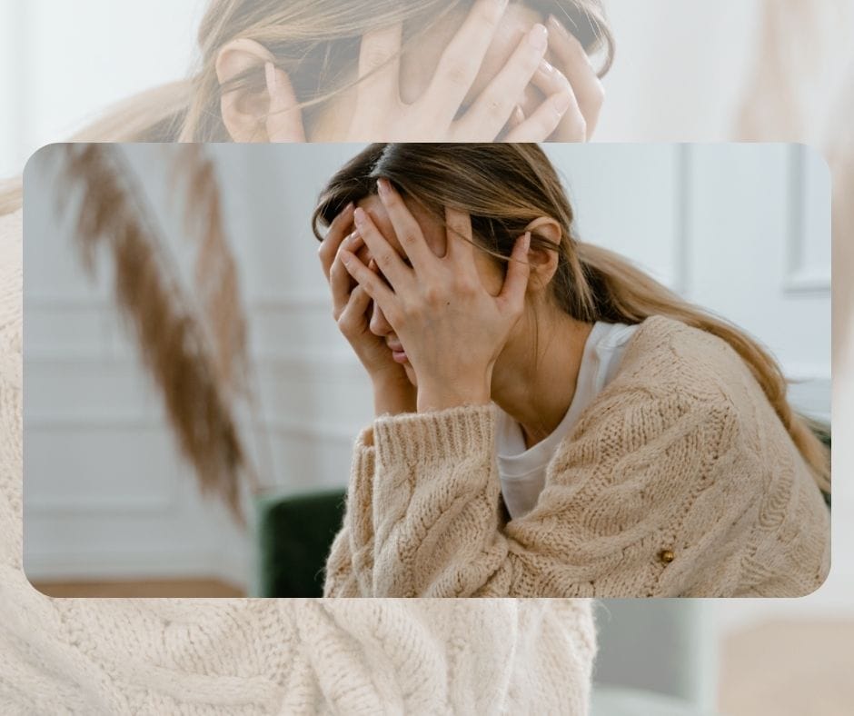 Una persona con cabello largo está sentada con la cabeza entre las manos, vistiendo un suéter de punto beige, en un interior, aparentemente sumida en una crisis existencial.