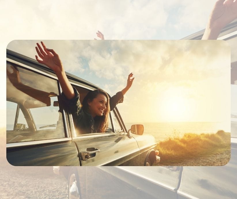 Persona asomada a la ventanilla de un coche con los brazos en alto, sonriendo, mientras el sol se pone cerca del océano, abrazando el momento y reflexionando sobre su propósito en la vida.