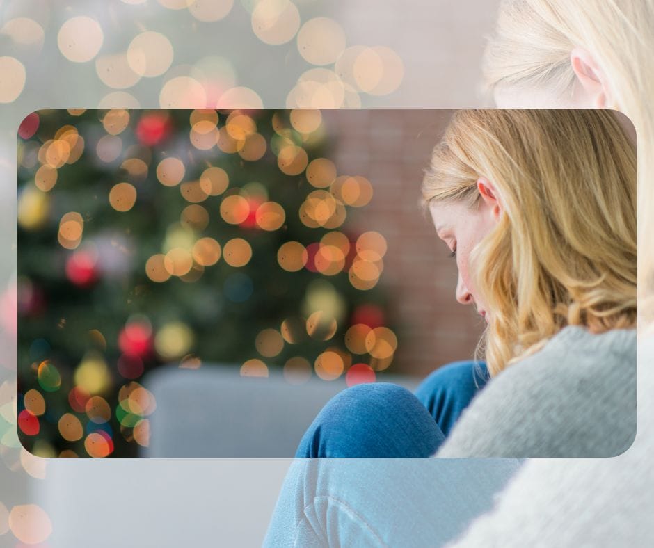 Una mujer se sienta tranquilamente con la cabeza sobre la rodilla, frente a un árbol de Navidad colorido difuminado por las luces, contemplando los conflictos familiares en Navidad. conflictos familiares en navidad